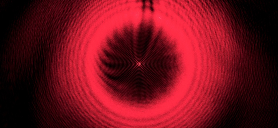 Figure shows a series of red concentric rings on a black background. At the center is a bright red spot.