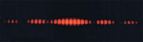 Figure is an image showing red interference pattern on a black background. The central part has brighter lines. The lines are cut off at the top and bottom, seemingly enclosed between two sinusoidal waves of opposite phase.